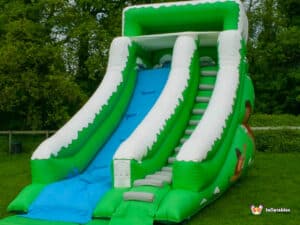 Large green and white inflatable slide, known as the Mammoth slide, towering against a clear blue sky.