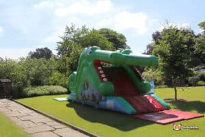 A large inflatable crocodile slide featuring a wide-open mouth, designed for children to enjoy outdoor play.