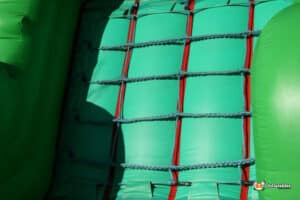 A vibrant green inflatable slide adorned with red and green ropes, inviting children to climb and slide down joyfully.