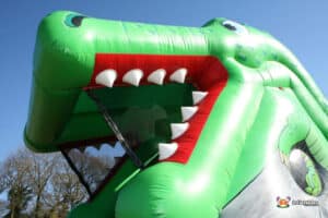 A large, bright inflatable crocodile slide in a garden, providing a playful attraction for children on a sunny day.