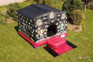 A colourful inflatable bouncy castle with disco-themed designs, set on green grass, featuring a Red entrance ramp.