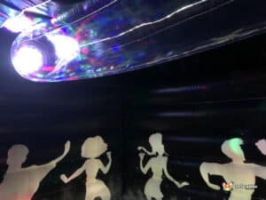 Inside a colorful inflatable party space, silhouettes of dancing people are illuminated by vibrant, swirling lights.