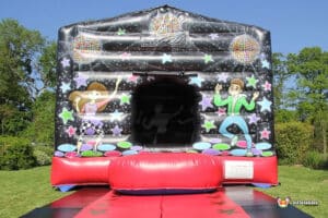 A colourful inflatable bouncy castle featuring cartoon dancers, vibrant stars, and disco balls, set in a green backyard.