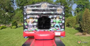 A colourful inflatable bouncy castle decorated with disco balls and cartoon characters, set in a grassy yard under clear blue skies.