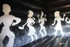 Silhouettes of dancers in various poses on a black background, creating a vibrant party atmosphere inside a bouncy castle.
