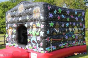 A colourful inflatable bouncy castle featuring disco themes, vibrant stars, and cartoon characters dancing, set in a grassy outdoor area.