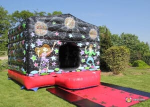 A colourful inflatable bouncy castle decorated with disco-themed designs and cartoon characters dancing under a starry sky.