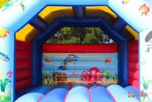 Brightly coloured inflatable bouncy castle featuring sea creatures like a dolphin and octopus, with a treasure chest and vibrant fish murals.