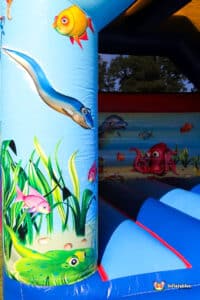 A colourful inflatable bouncy castle featuring ocean-themed graphics, including fish, an octopus, and underwater plants.