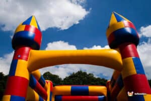 Colorful inflatable bouncy castle with castle towers under a bright blue sky, surrounded by greenery. Fun and playful atmosphere.