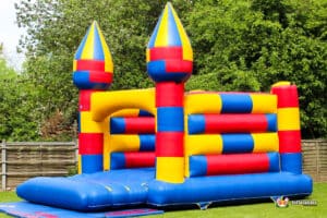 A colorful inflatable bouncy castle with red, yellow, and blue sections, set up outdoors against a backdrop of green trees.