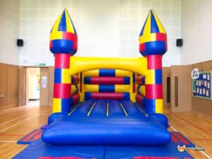 Brightly colored inflatable bouncy castle with blue, red, and yellow sections, set up indoors in a spacious play area.