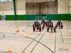 Multiple go-karts positioned in a gymnasium, featuring various colors and styles, awaiting drivers.