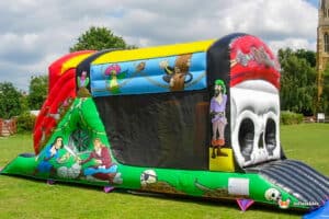 Colorful pirate-themed inflatable bouncy castle with characters, swords, and a skull design, set on a grassy area under a cloudy sky.