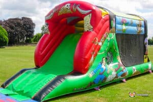 A vibrant inflatable pirate themed fun run with a steep green slide, adorned with colorful pirate illustrations and skull designs.