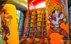 Brightly colored inflatable bounce house entrance featuring pirate-themed decorations, including a skull, coins, and vibrant rainbow hues.
