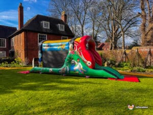A colourful inflatable pirate-themed fun run with a slide, set on green grass near a brick house and trees.