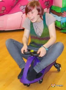 a young girl joyfully riding in a small toy car, smiling as she enjoys a playful adventure.