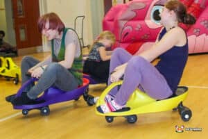 young girls joyfully riding together in a small toy car, smiling as they enjoy their playful adventure