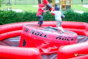 Two boys engage in a playful duel on an inflatable gladiator arena, showcasing their competitive spirit and fun.