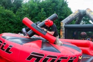 A man rides on an inflatable gladiator duel, balancing on a colorful obstacle while preparing for a friendly competition.