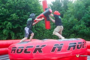 Two men joyfully challenge each other on an inflatable gladiator duel, immersed in a spirited game.