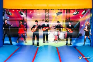 A colorful bouncy castle interior features cartoon musicians performing on stage, surrounded by lights and vibrant decorations.