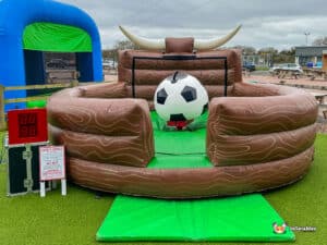 A bull-riding inflatable game featuring a football ball in the centre, surrounded by padded walls and a green turf floor.