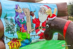 A festive inflatable display features Santa, an elf with a scroll, and a reindeer wearing a red Santa hat, surrounded by Christmas gifts.