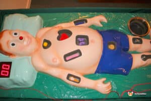 A person assists a baby with a Sawbones Electronic Operation Game, demonstrating interactive play and learning.
