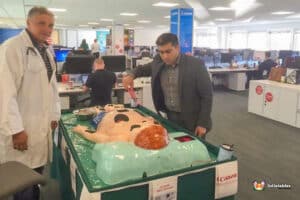 Two men in white coats examine a mannequin in the context of the Sawbones Electronic Operation Game.