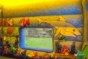 A large inflatable bouncer designed with a shark and fish theme, featuring vibrant colors and playful ocean graphics.