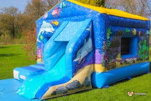 A lively bouncy castle adorned with fish motifs and a slide, providing a fun play area for children at a festive gathering.