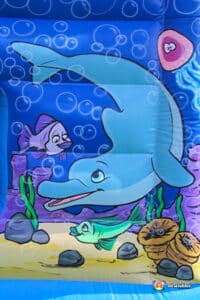 A vibrant inflatable bouncer featuring a dolphin and fish, perfect for children's outdoor play and summer fun.