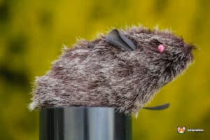 A plush toy rat featuring a soft body and a distinct pink nose, sitting on a colorful background.