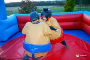 Two kids in sumo suits enjoy a playful match in an inflatable boxing ring set on a large inflatable arena.