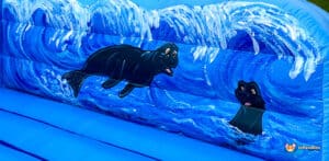 A bright blue inflatable with playful cartoon manatees and wave designs, creating a fun aquatic theme for kids.