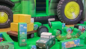 A colorful play area filled with toys, prominently showcasing a B&S Deluxe Package tractor for kids to play with.