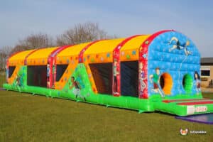 A colourful inflatable ultimate obstacle course featuring various sports-themed designs, set on a grassy area under a clear sky.