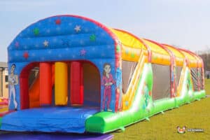 A colourful inflatable ultimate obstacle course adorned with stars and cartoon characters, set on a grassy outdoor area, inviting playful activities.