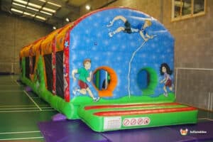 A colorful inflatable obstacle course featuring playful designs of children running and climbing, set up indoors on a gym floor.