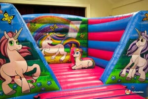 A colourful unicorn-themed bouncy castle with vibrant graphics of unicorns, butterflies, and rainbows on blue and pink inflatable walls.