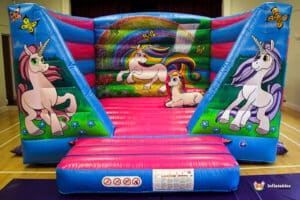 A colourful unicorn-themed bouncy castle with vibrant designs of unicorns and butterflies, set in a playful indoor space.