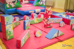 A cheerful low unicorn-themed bouncy castle with an assortment of soft play toys for children's entertainment.