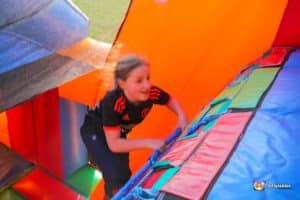 A child climbs a colourful inflatable structure, surrounded by bright orange and green panels, enjoying a day of play and fun.