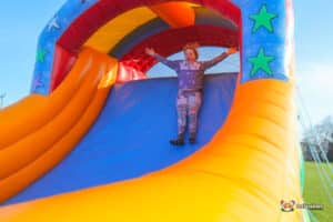 A child joyfully slides down a colorful inflatable slide with stars, set against a clear blue sky.