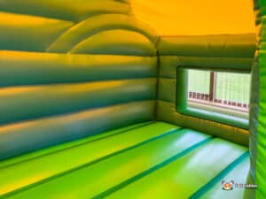 A green and yellow inflatable bouncer shaped like a tractor, featuring a large window for visibility.