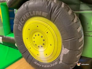 A vibrant green tractor sits atop a large inflatable tire, creating a fun and whimsical outdoor display.