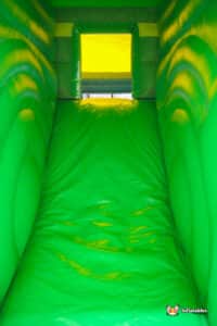 A vibrant green inflatable bouncer featuring a colorful slide, inviting children to play and have fun.