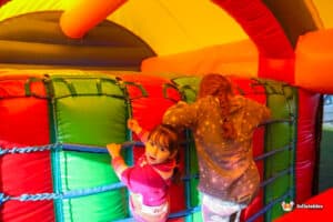 A young girl slides down 'The Colossal' inflatable slide, embodying joy and excitement in a colorful playground environment.